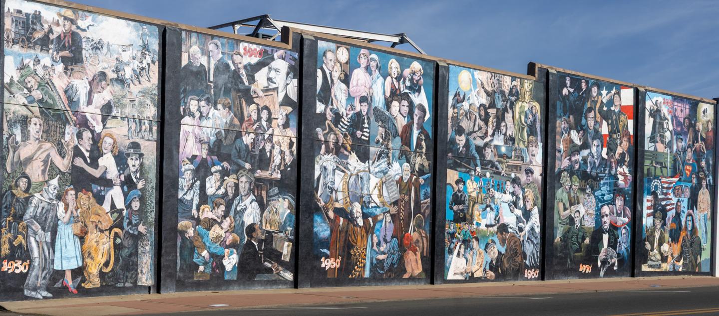 Six tall panels covered in colorful graffiti murals against a cloudy sky.