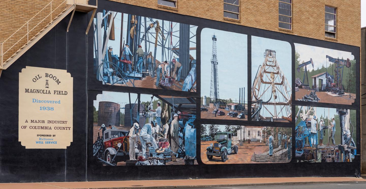 Brick storefront with large mural-style windows showing industrial scenes.