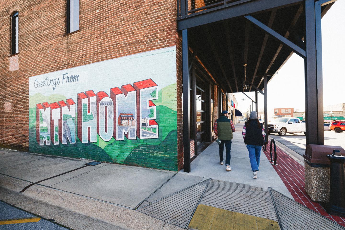 Mural reading “Welcome Home” beside a sidewalk under elevated tracks.