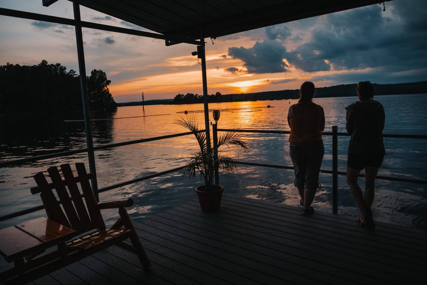 Two people watch a sunset over the ocean from a covered deck.