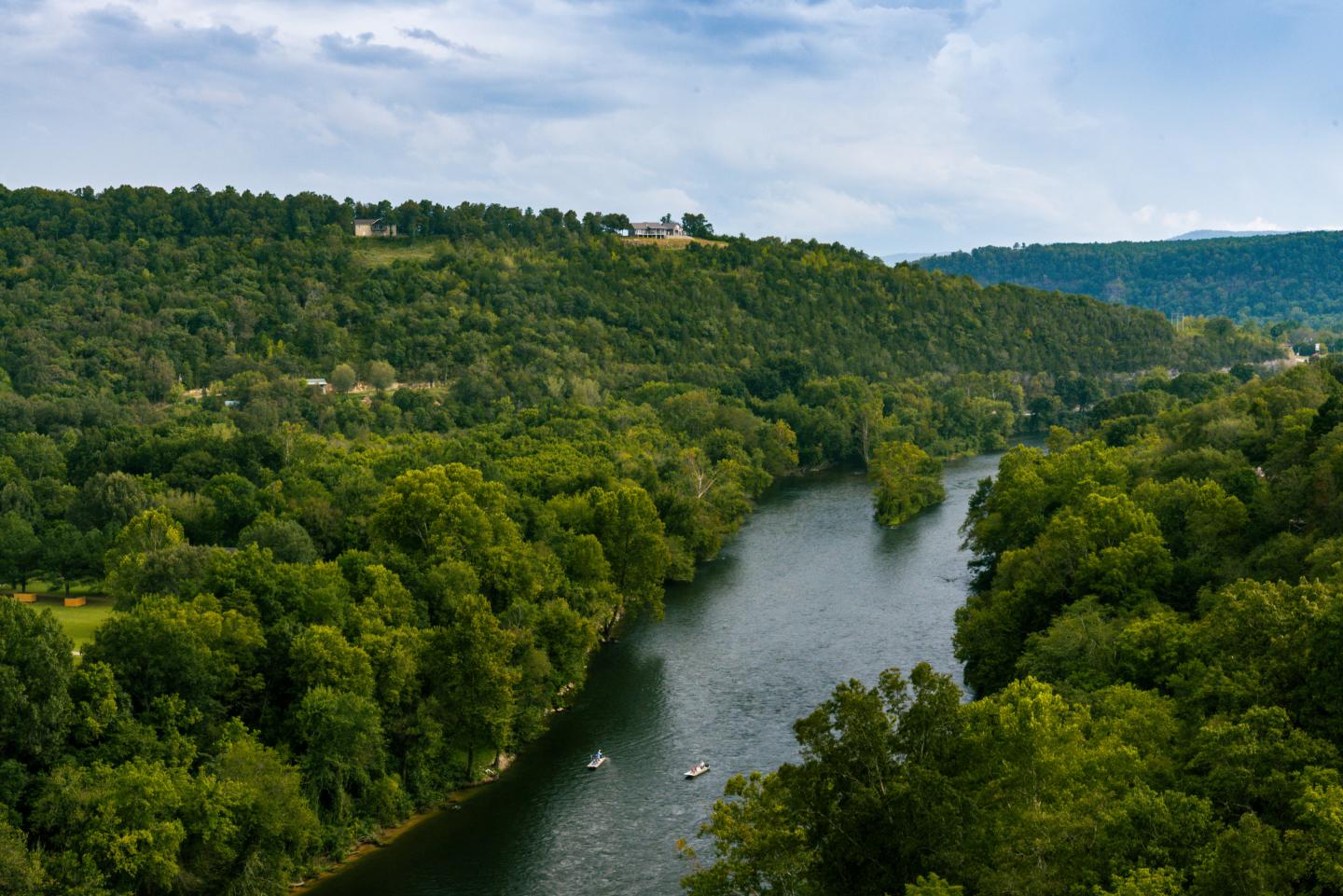 A winding river flowing through dense green forest beneath a cloudy sky
