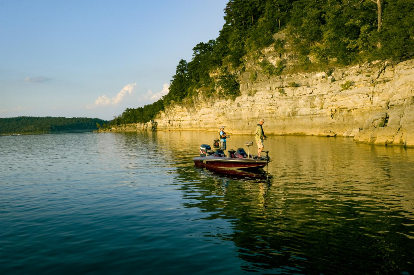 Kayaker paddles beside a sunlit limestone cliff on calm water.