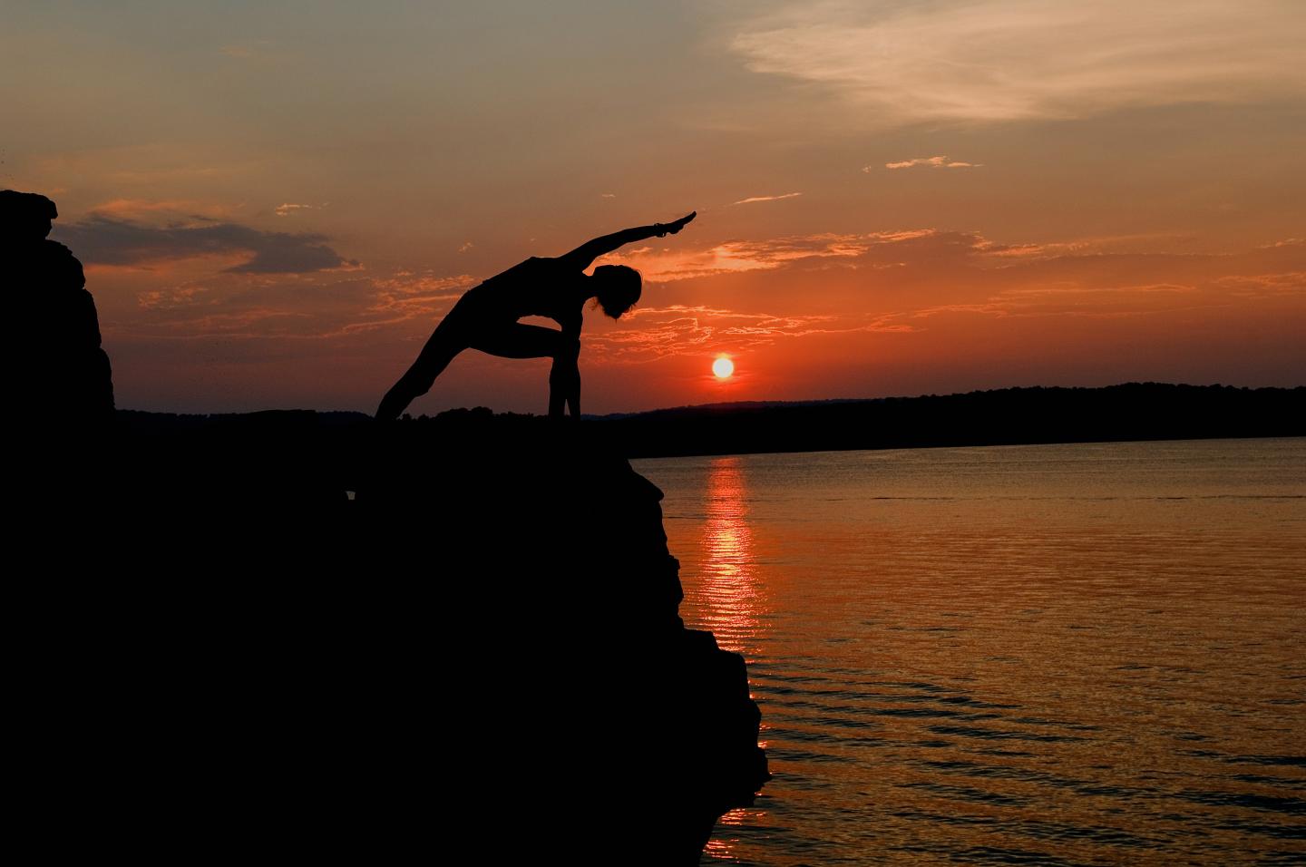 Silhouette of a person diving from a cliff into a sunset-lit lake