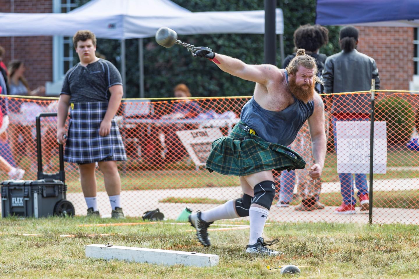 Athlete in kilt throws a weight at a Highland games field.