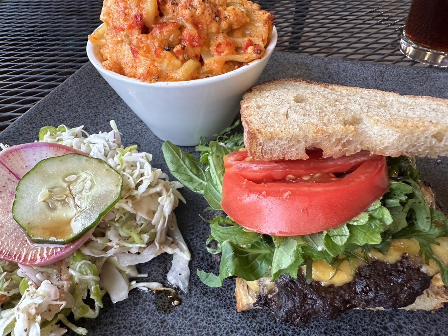 Vegetarian burger with tomato, lettuce, sprouts, pickle, and a side of pasta salad