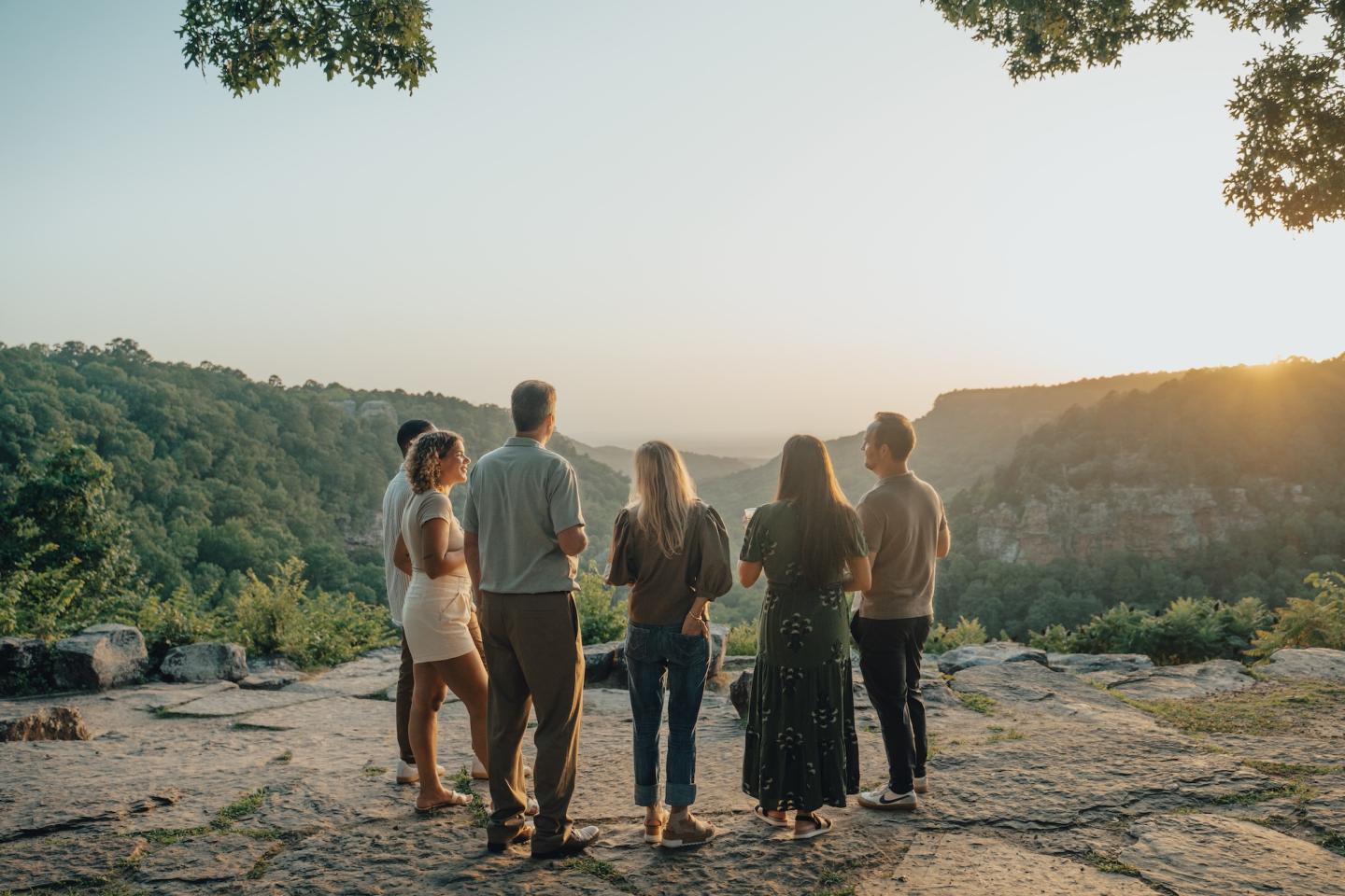 Five friends stand together in a rocky clearing at sunset.