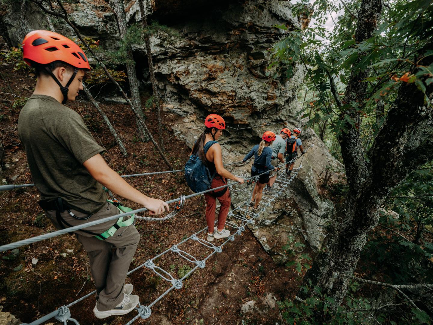 Three climbers in helmets rappelling down a rocky forest cliff.