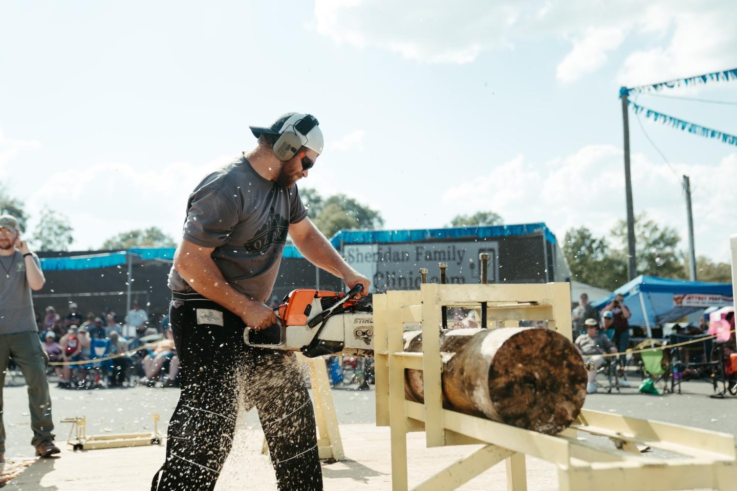 Man using a chainsaw to carve a log at an outdoor fair.