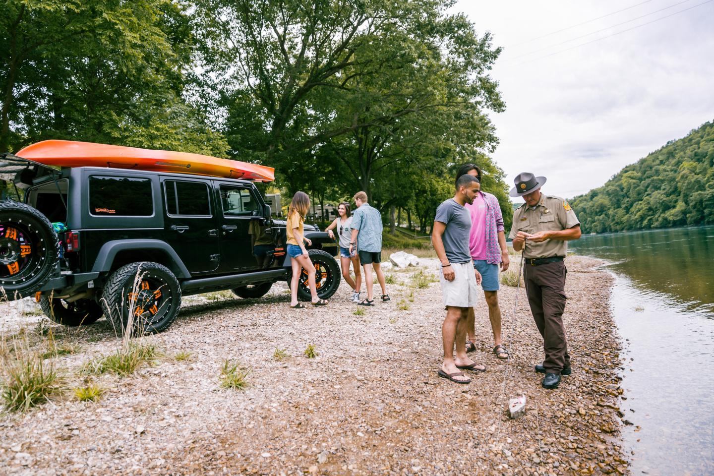 Group of friends with a vintage SUV by a lakeside shore.