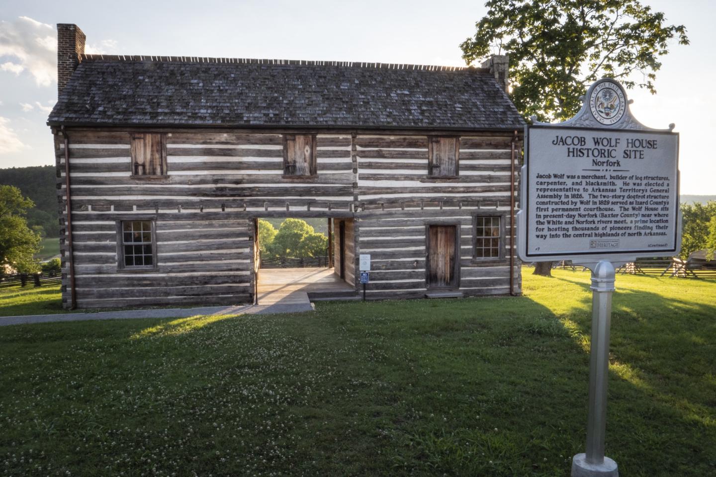 Historic log cabin with a roadside historical marker on a grassy lawn.