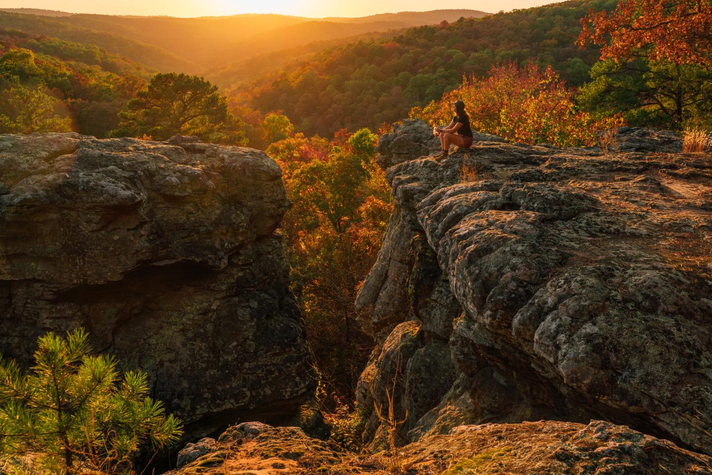 Sunset over rocky canyon cliffs with autumn trees and a distant river.