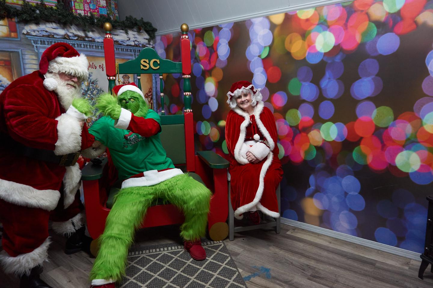 Santa and the Grinch posing with a gift beside a festive balloon wall