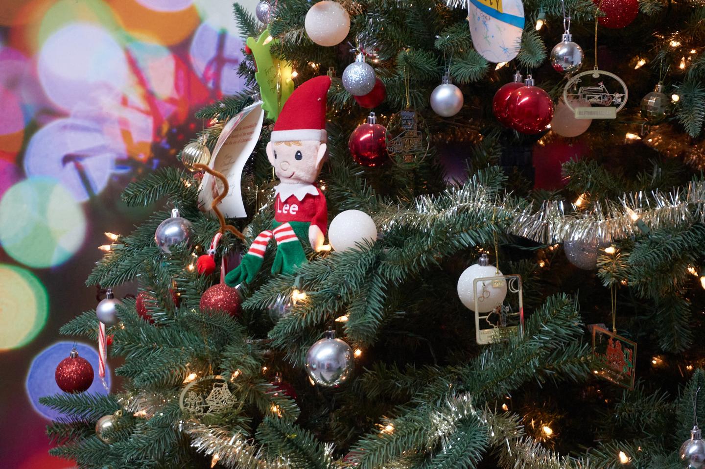 Christmas tree with red ornaments, lights, and a Santa elf decoration