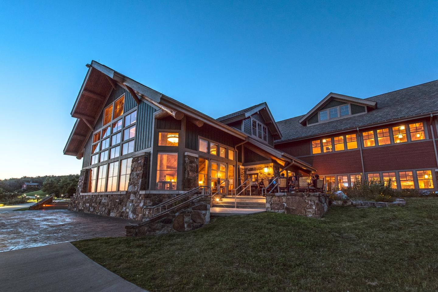 Large timber lodge glowing warmly at dusk beneath a blue sky.