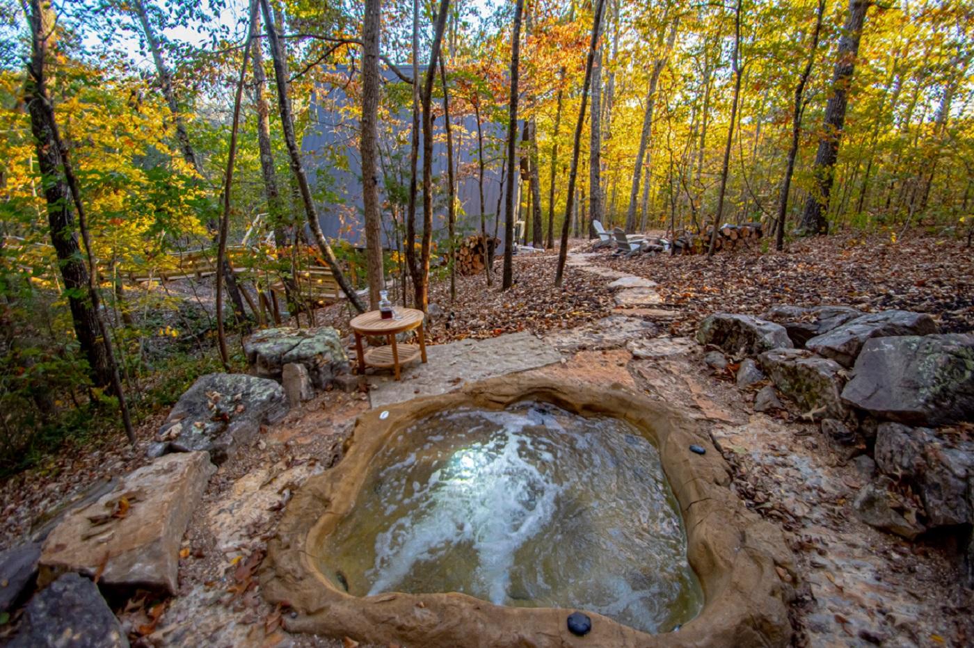 Small bubbling hot spring in a forest clearing with autumn trees.