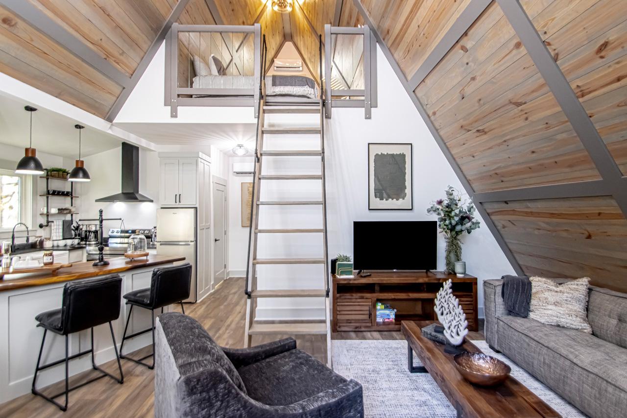 Cozy modern loft living room with vaulted wood ceiling, ladder, and open kitchen.