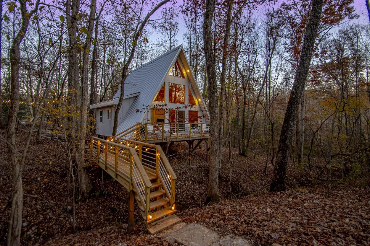A-frame cabin with lit interior and wooden stairs in an autumn forest