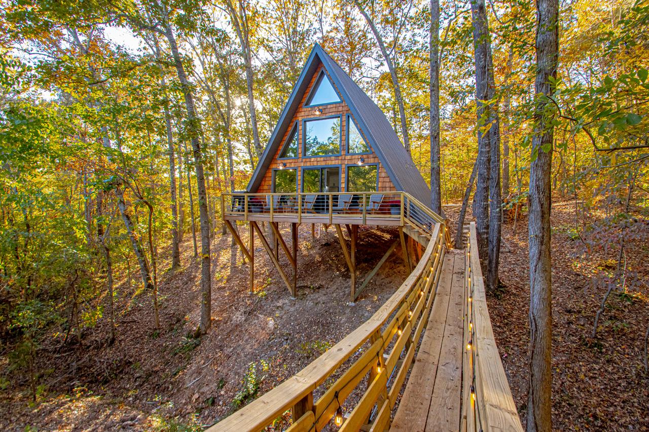 A-frame cabin in autumn woods, reached by a wooden boardwalk.