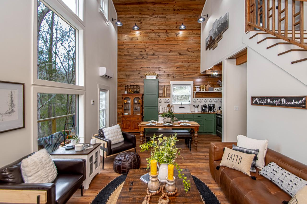 Warm wood-paneled living room with tall windows, leather sofas, and staircase.