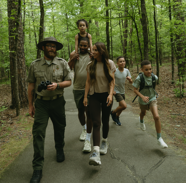 Forest ranger leading a group of young hikers along a wooded trail.