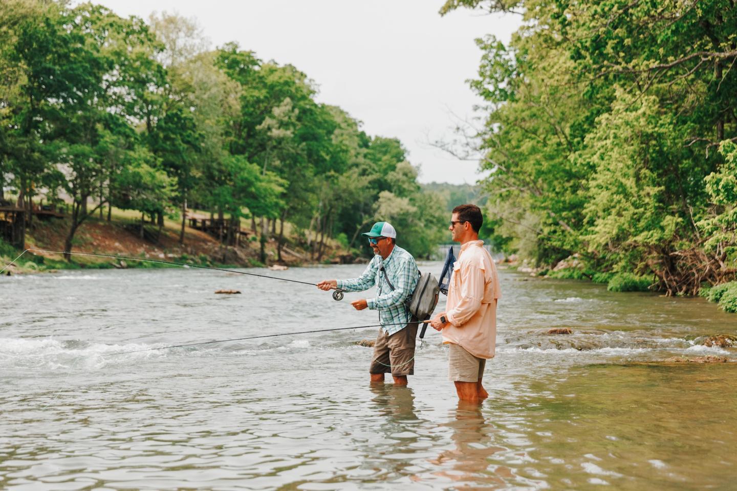 Two people fly fishing in a shallow, tree-lined river.