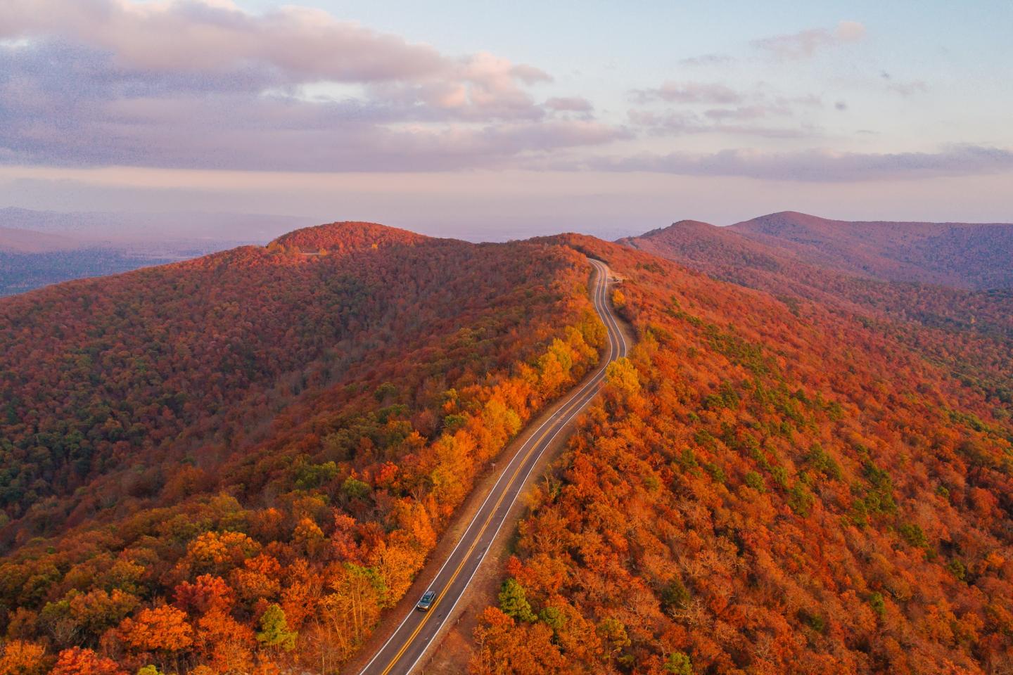 A winding road through vibrant autumn forested mountains at sunset