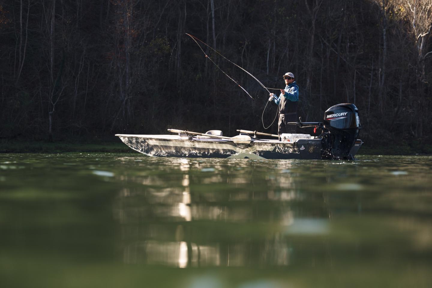 Angler standing on a small boat on a calm river, reflected in green water.
