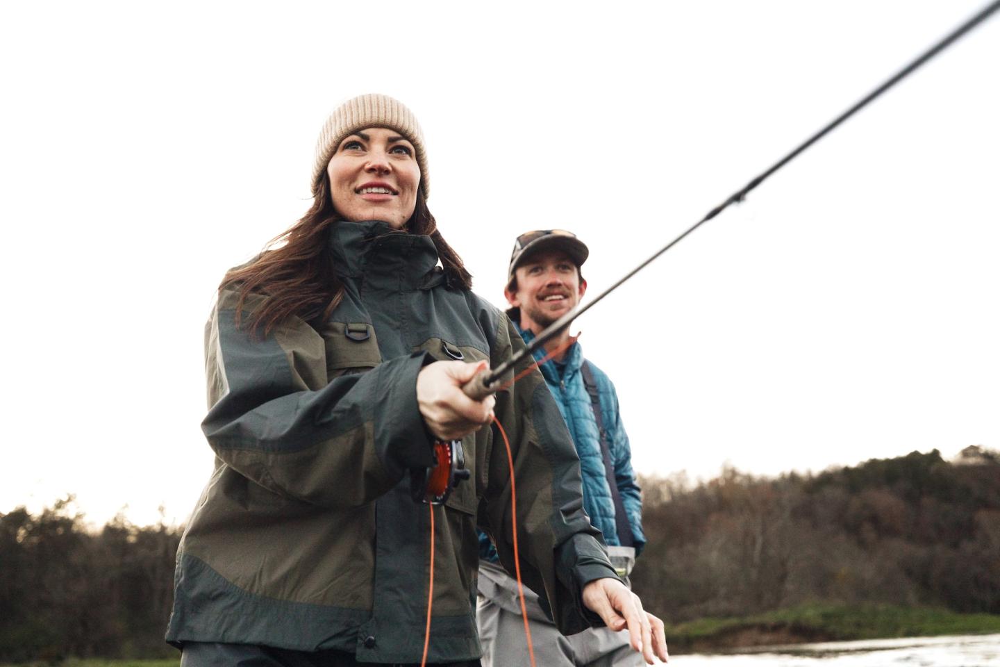Woman and man fishing together by a lakeshore.