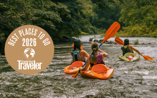 Kayakers paddling down a forested river with an award badge on the side.